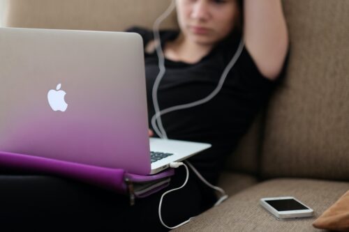 A young woman sits on the couch and looks at a laptop