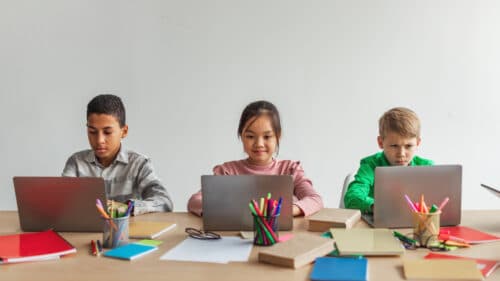 Three multiracial school kids using laptops learning