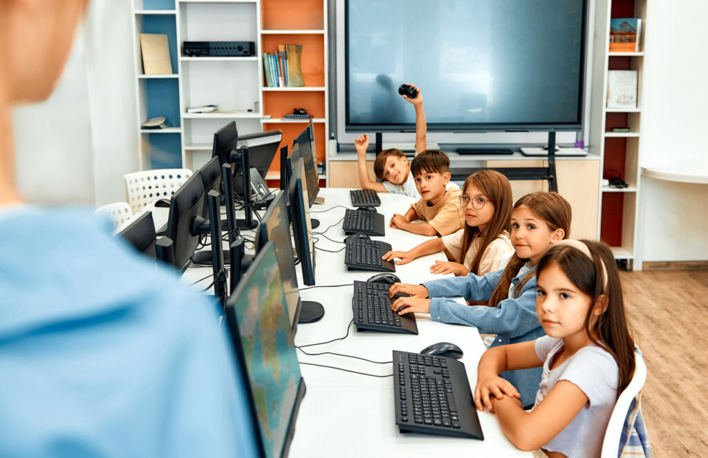 Group of children sit at desks with computers