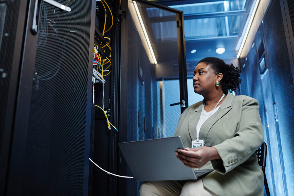 Woman sits in a data center and sets up network segmentation with her laptop